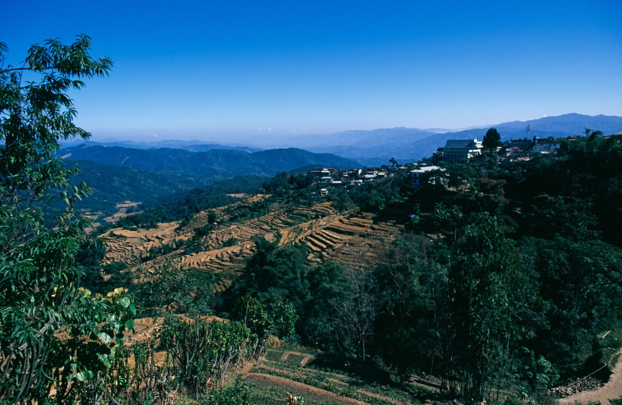 Hilltop town of tin-roofed houses above cut terrace fields and hazy blue ranges